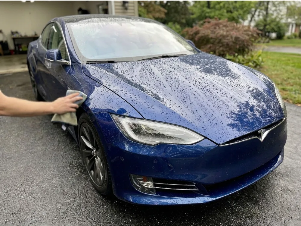Detailer wiping down a blue Tesla with water beading on the ceramic coated paint