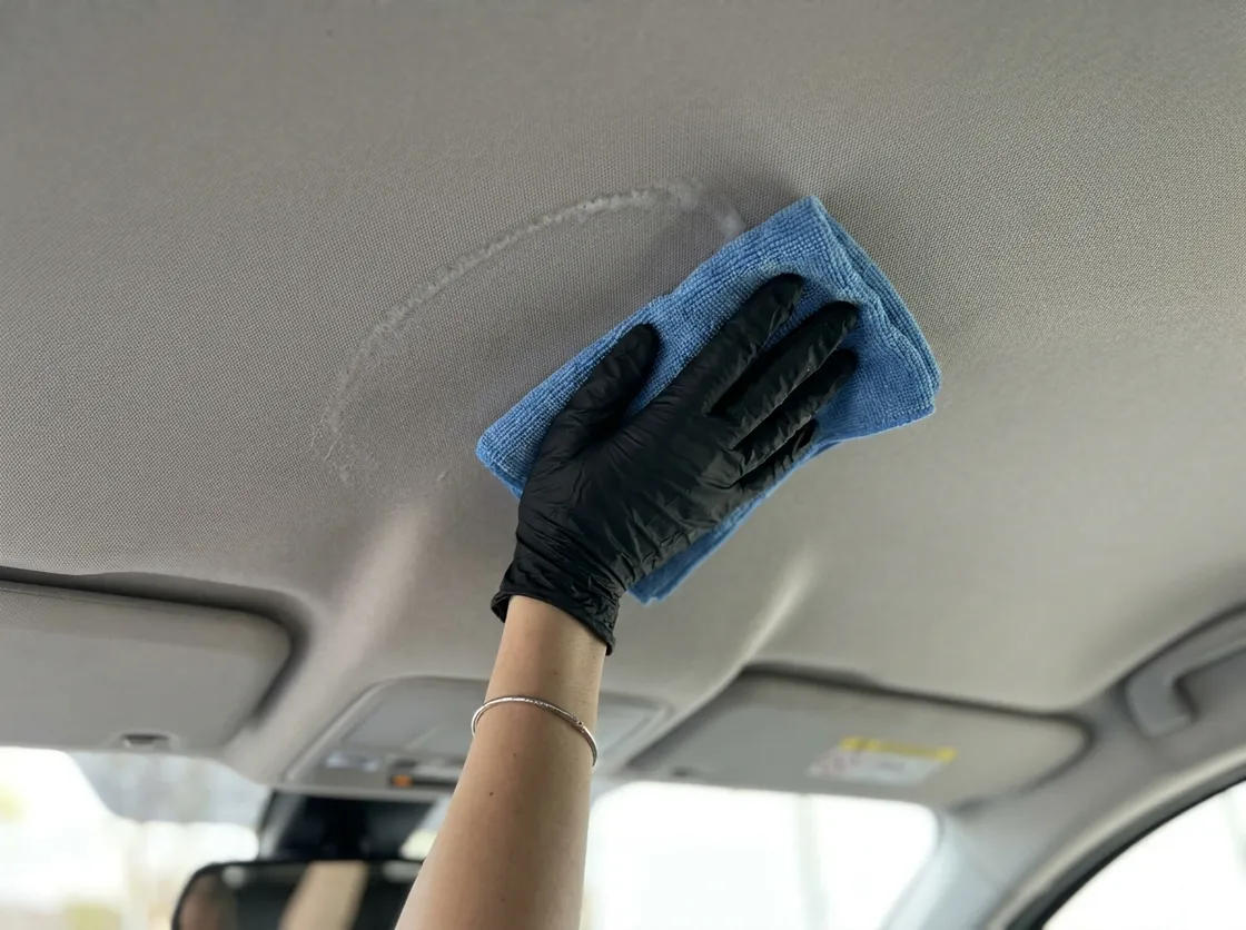 Gloved hand cleaning a car headliner with a blue microfibre cloth