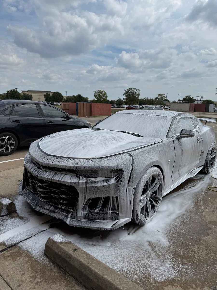 Black Chevrolet Camaro ZL1 covered in snow foam during a mobile wash