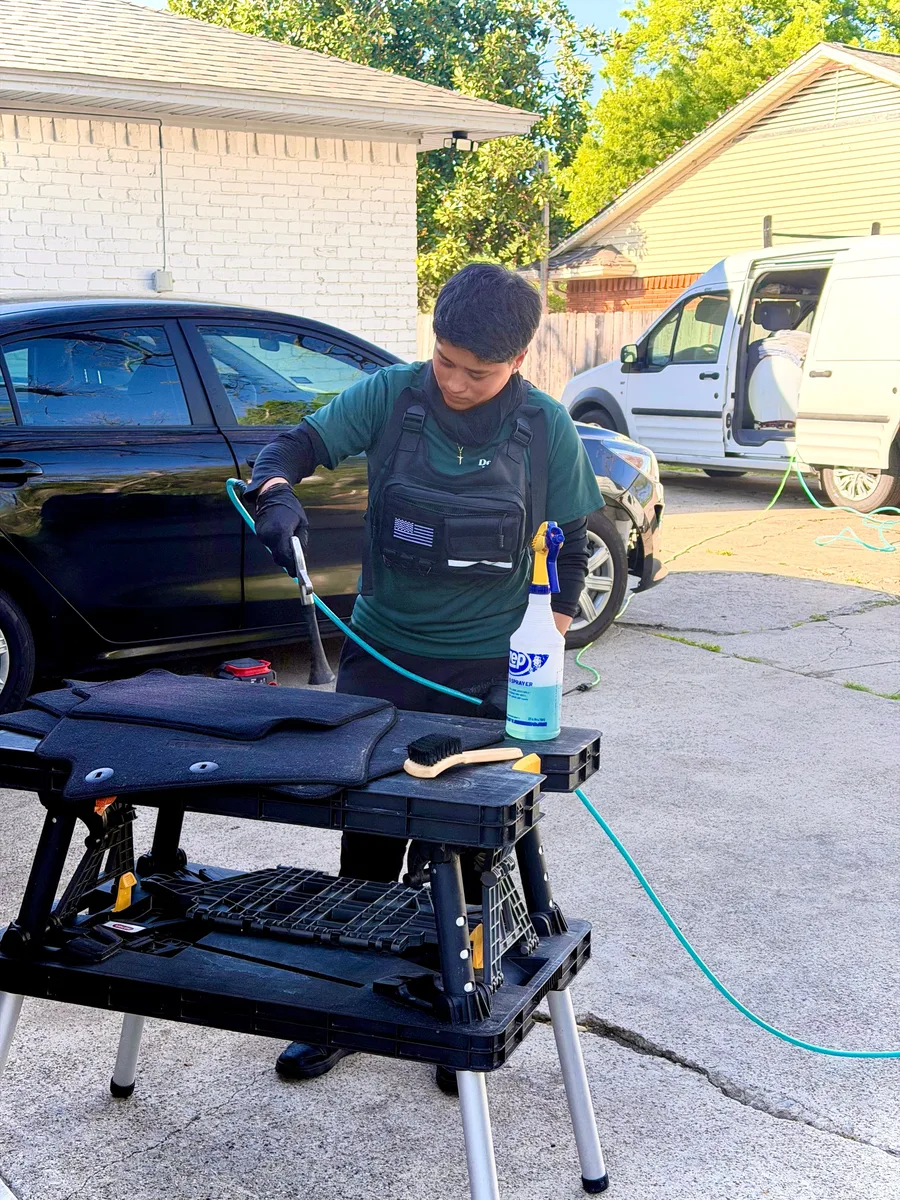 Auto Detailing Pro technician steam cleaning floor mats on a portable table next to the mobile detailing van